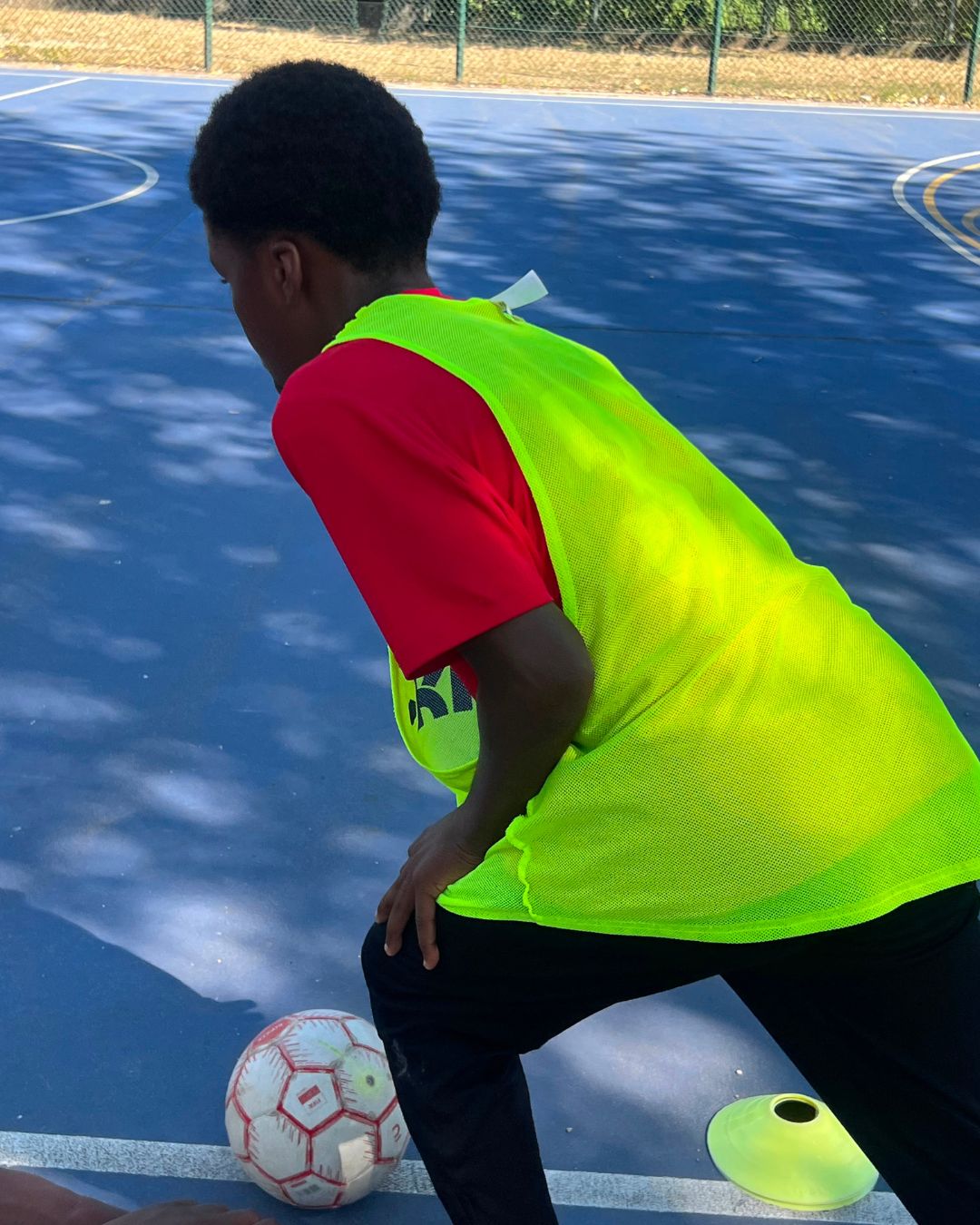 Jovem com colete verde a jogar futsal